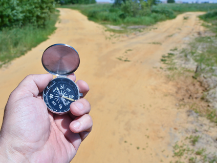 Hand holding a compass at a forked path, symbolizing strategic financial decision-making and long-term direction.